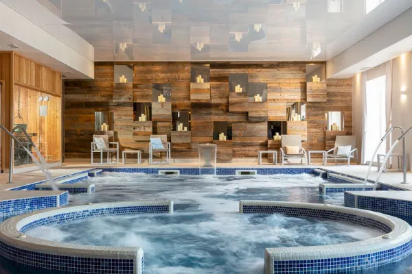 Indoor spa area with a circular bubbling hot tub, wooden lounge chairs, and decorative wooden wall with candles.