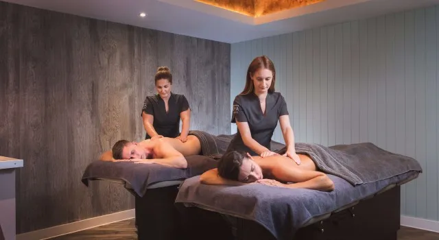 Two people receiving massages from therapists in a spa room