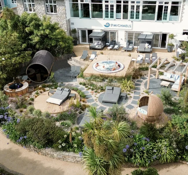 Outdoor spa area with hot tub, sun loungers, garden seating, and lush greenery at St Michaels.