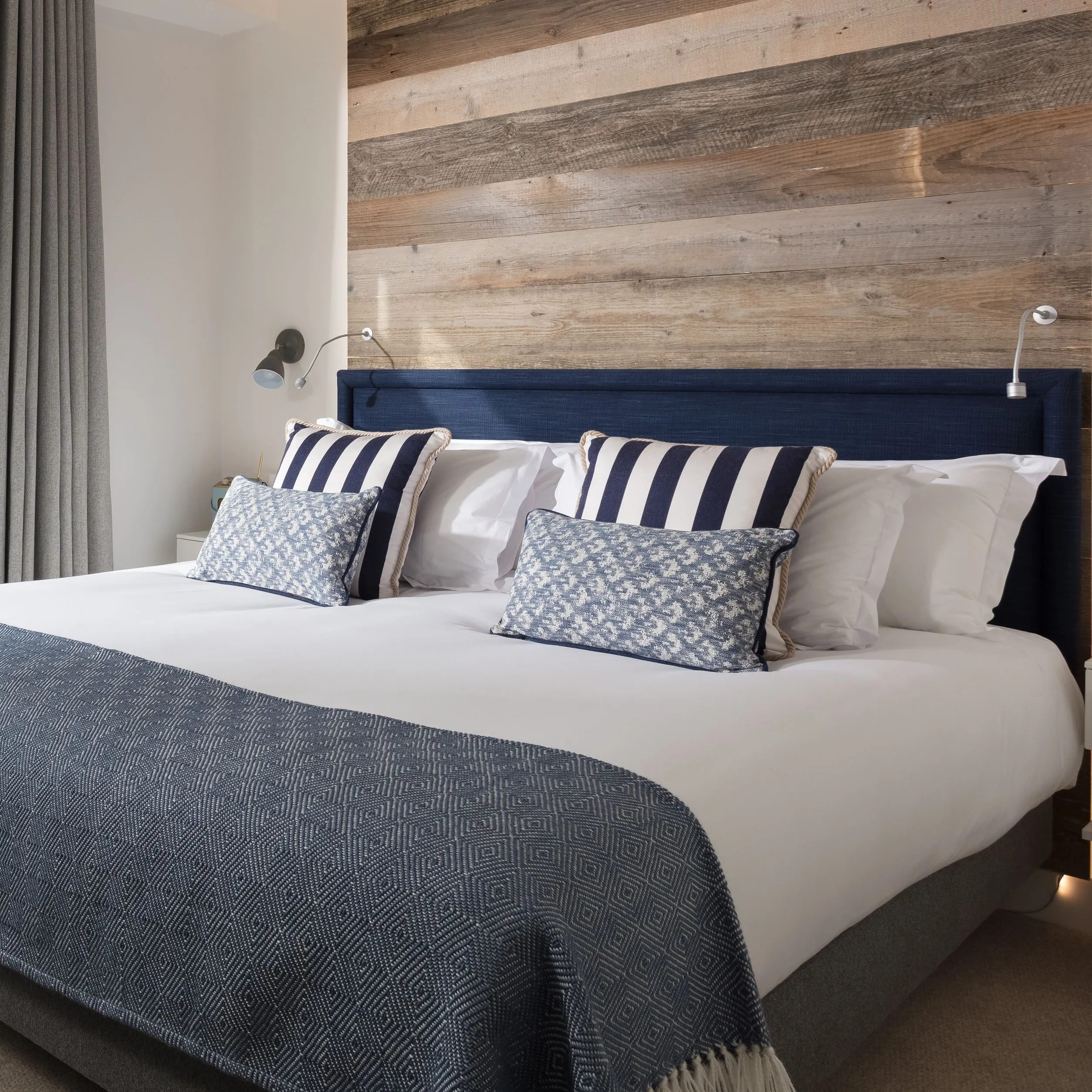Modern beach house room with large bed, wooden accent wall, and terrace overlooking greenery.