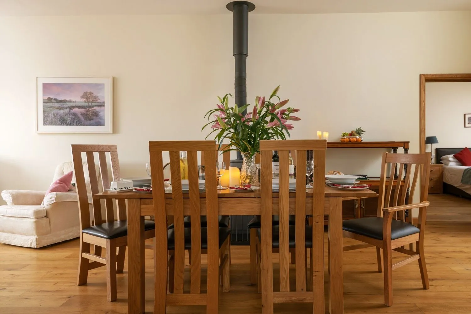Open-plan dining area at Glenside with wooden table, tall chairs, flowers and a central wood-burning stove