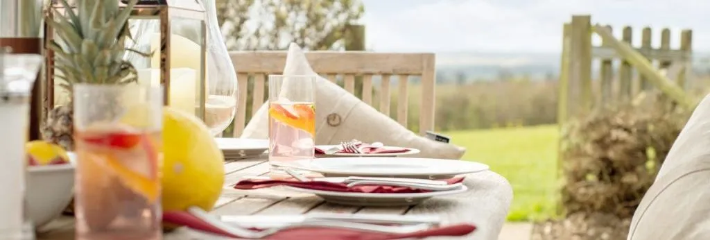 Outdoor dining table set with plates, red napkins, fruit and drinks in a garden setting