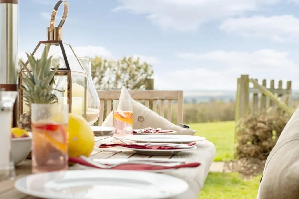 Outdoor dining table set with plates, red napkins, fruit and drinks in a garden setting
