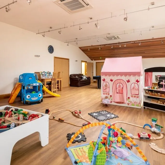Spacious indoor children's playroom with wooden floors, a play tent, toy bus slide, train set and play theatre