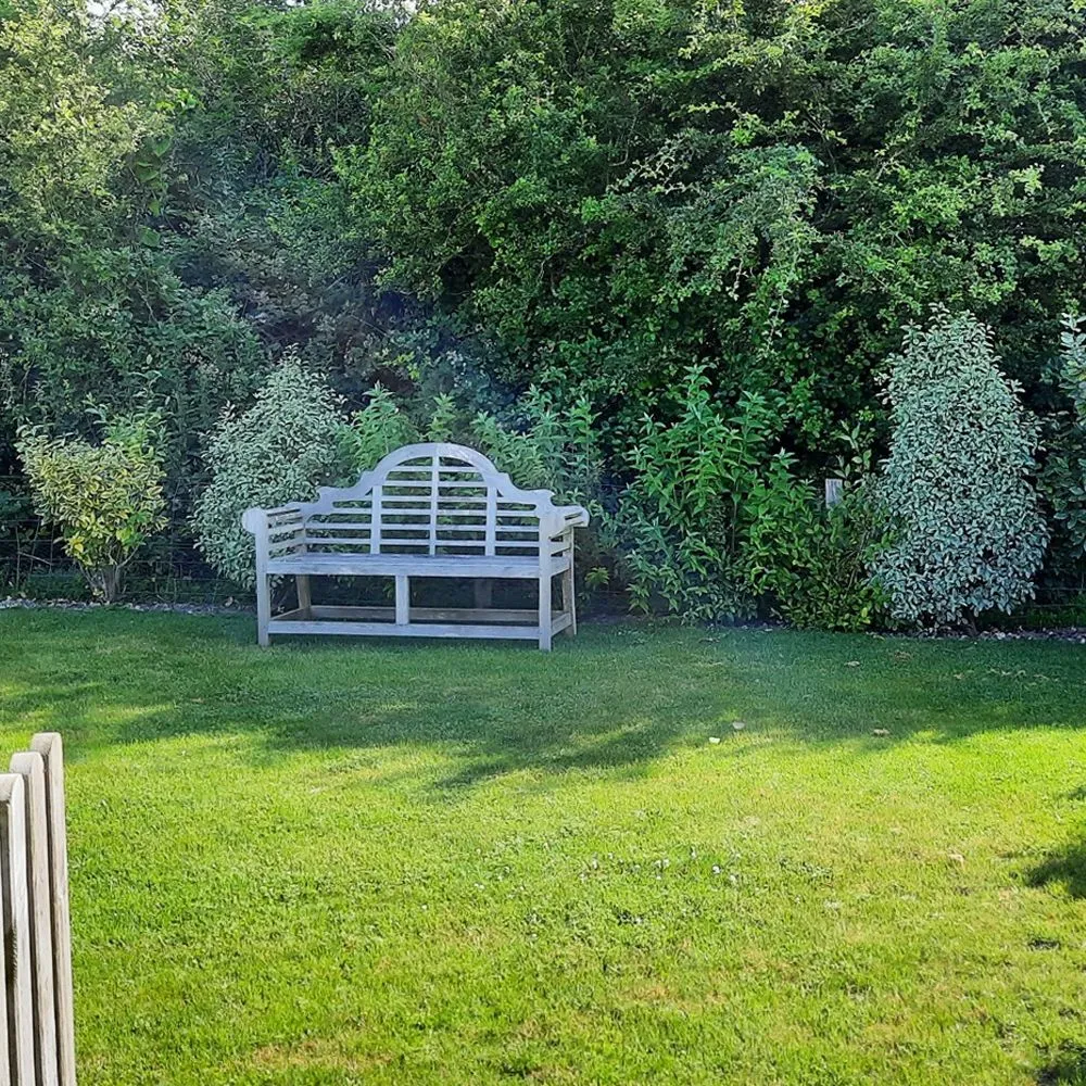 Enclosed garden with a neatly kept lawn, mature shrubs and a wooden bench