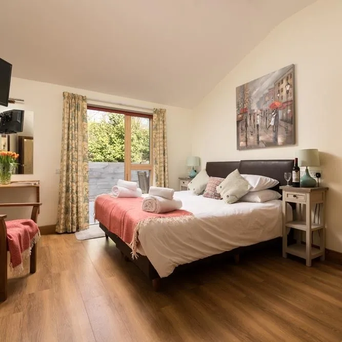 Bright double bedroom with wooden floor, bedside tables, TV, wardrobe and patio doors opening to a garden area