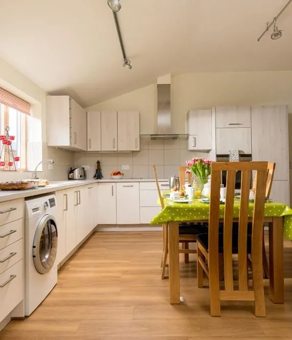 Bright open-plan kitchen and dining area with light wood units, dining table and sofa