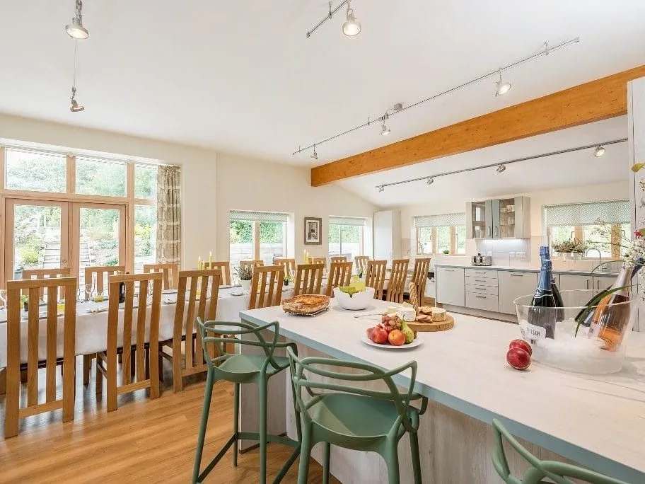 Spacious open-plan kitchen and dining area with a large island, wooden chairs, high ceilings and floor-to-ceiling windows.