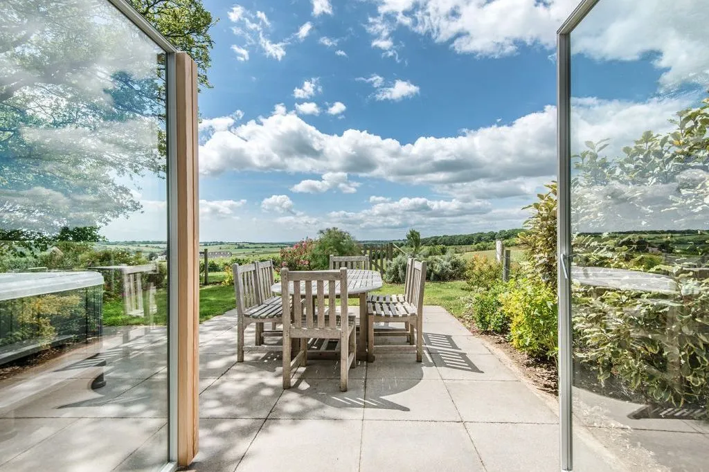 Patio view at Glenside Cottage with outdoor dining furniture, hot tub and countryside beyond