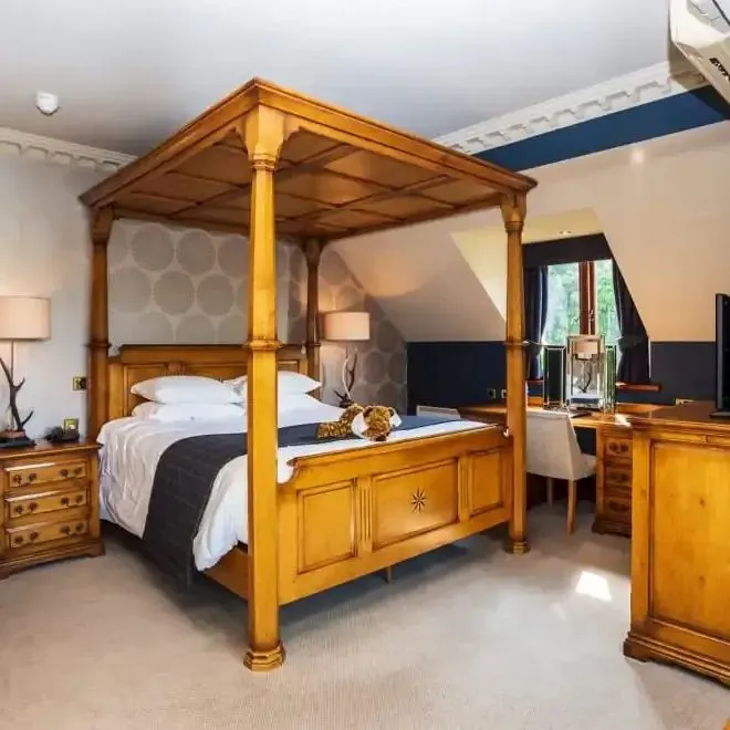 Spacious bedroom with a wooden four-poster bed, bedside tables, desk area and television