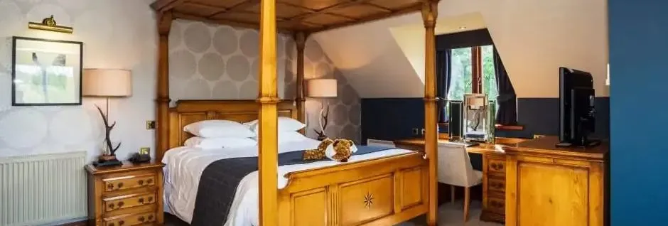 Spacious bedroom with a wooden four-poster bed, bedside tables, desk area and television