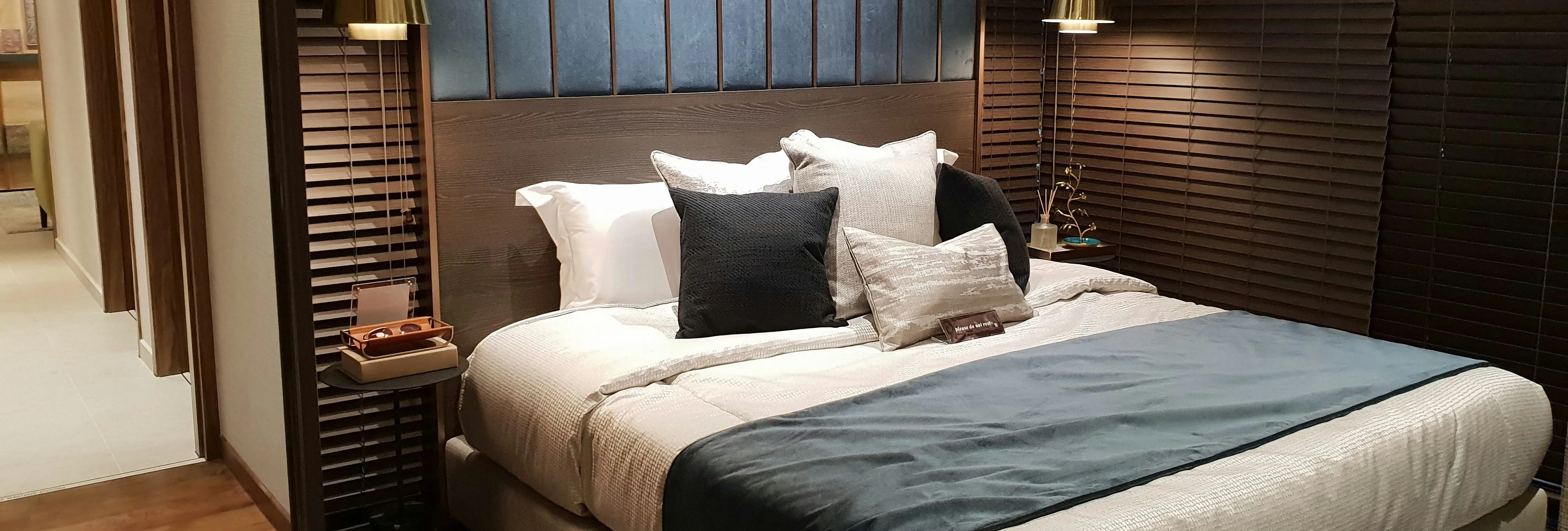 Modern bedroom with a neatly made double bed, dark wood blinds, and warm pendant lighting