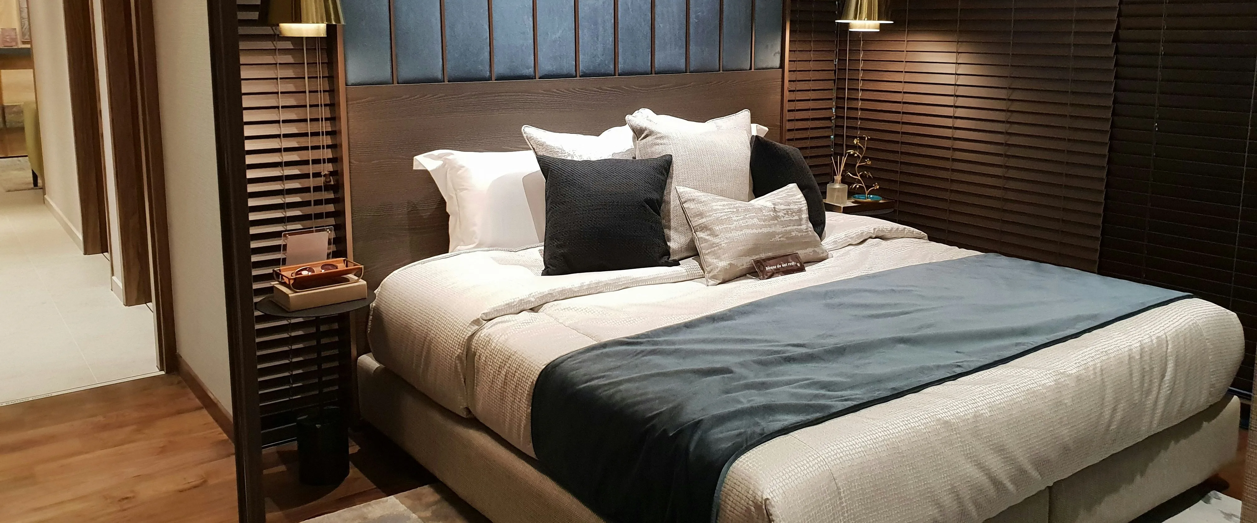 Modern bedroom with a neatly made double bed, dark wood blinds, and warm pendant lighting