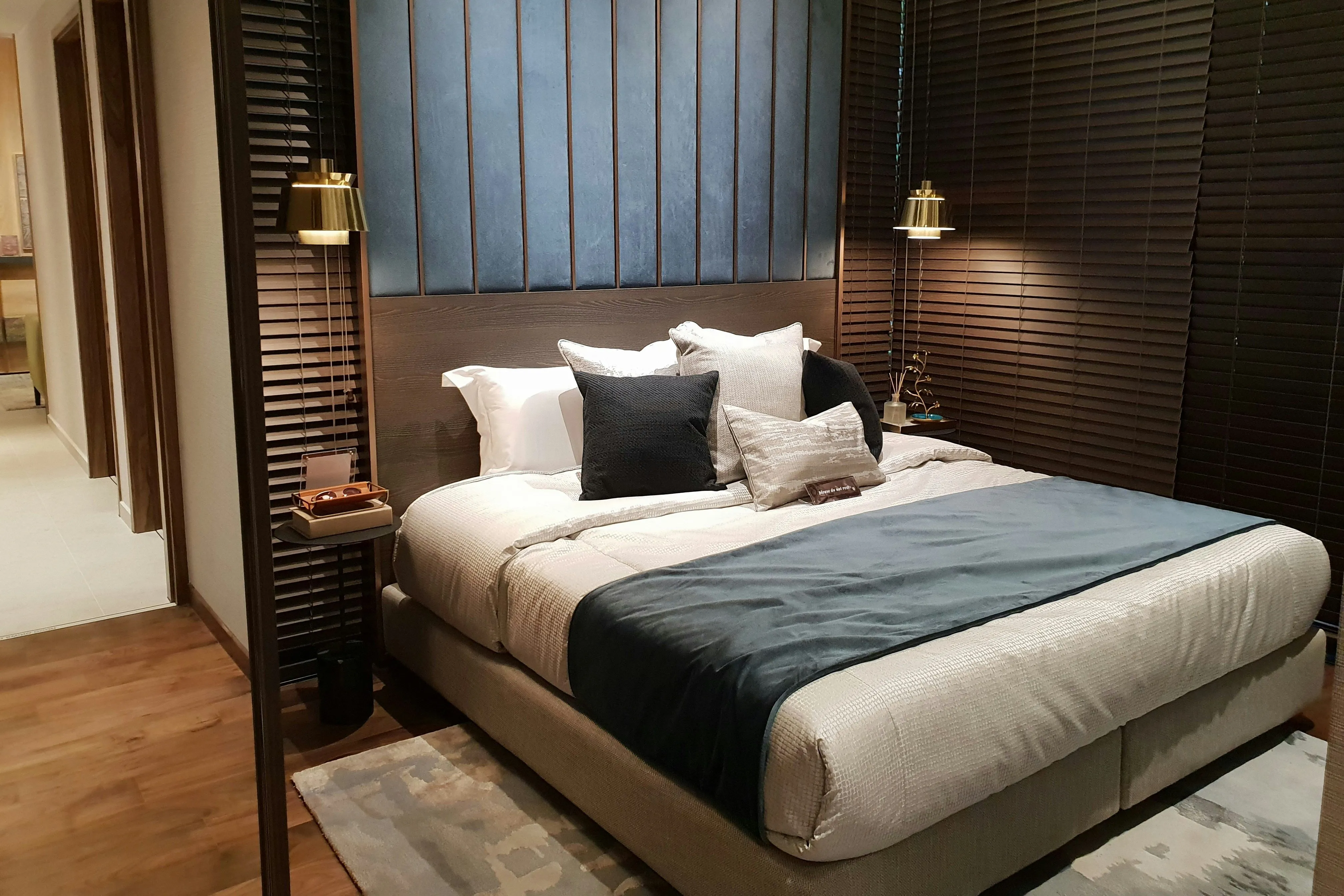 Modern bedroom with a neatly made double bed, dark wood blinds, and warm pendant lighting