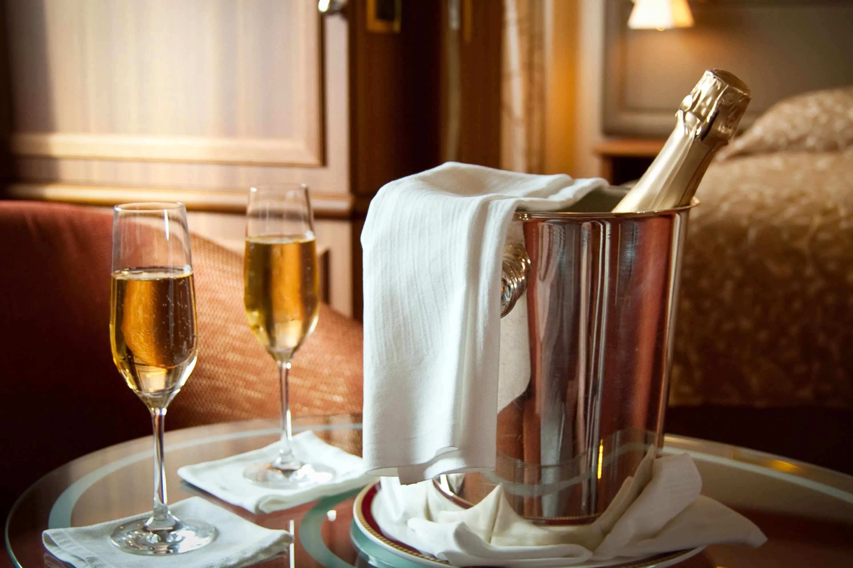 Bottle of sparkling wine in an ice bucket with two filled flutes on a table in a hotel bedroom