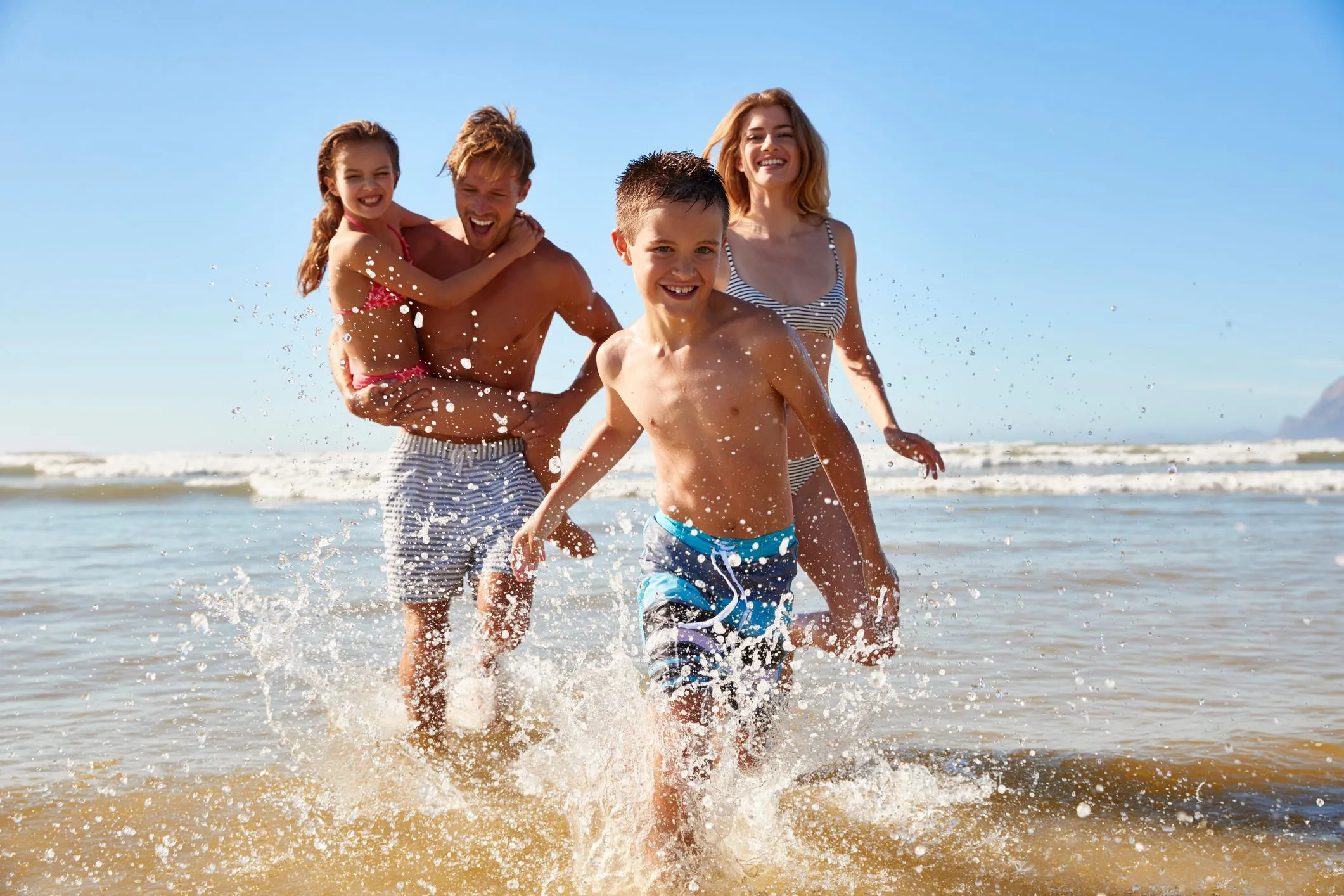 Family running and splashing in shallow sea water on a sunny beach