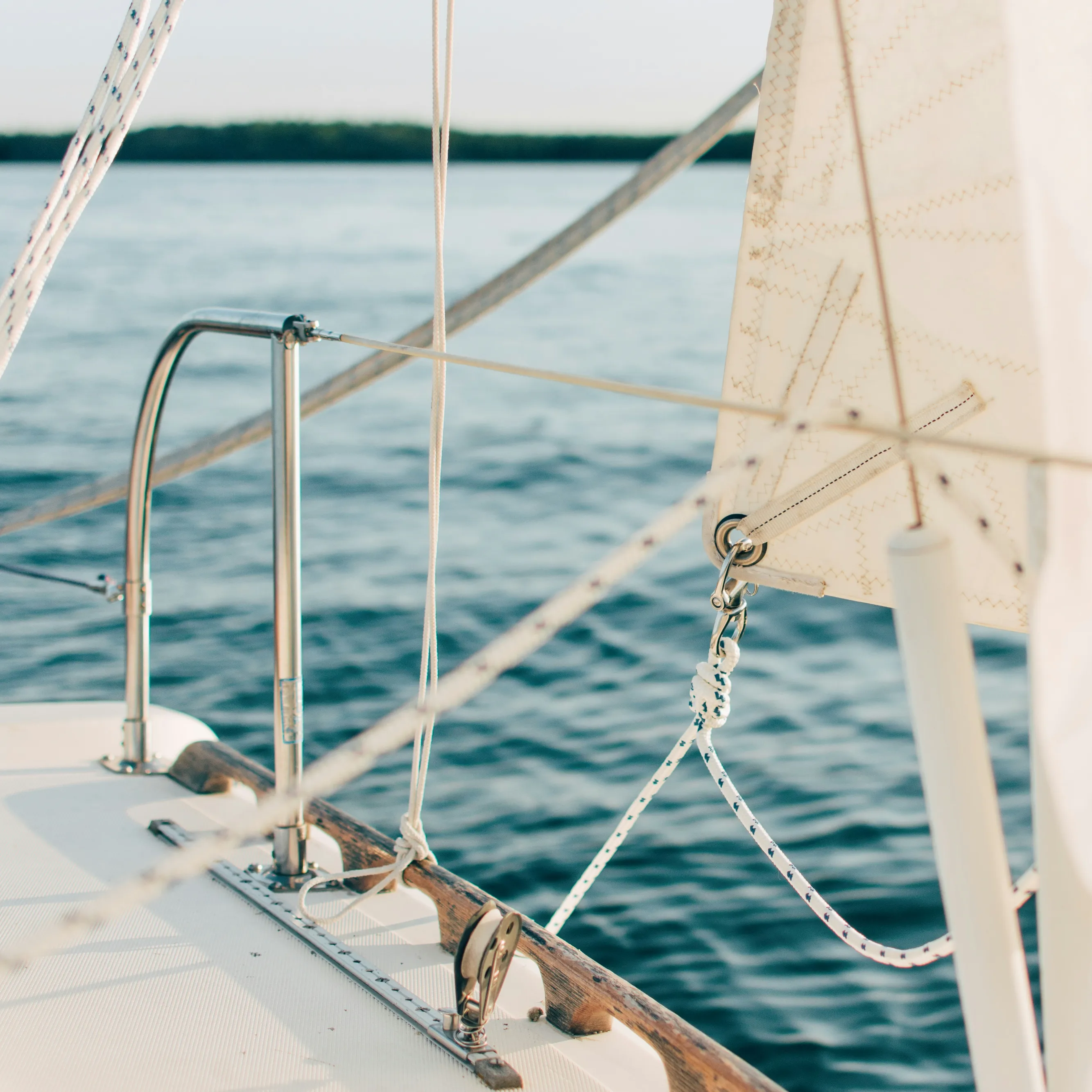 Close-up of a sailboat deck and rigging with cream sails above calm blue water.