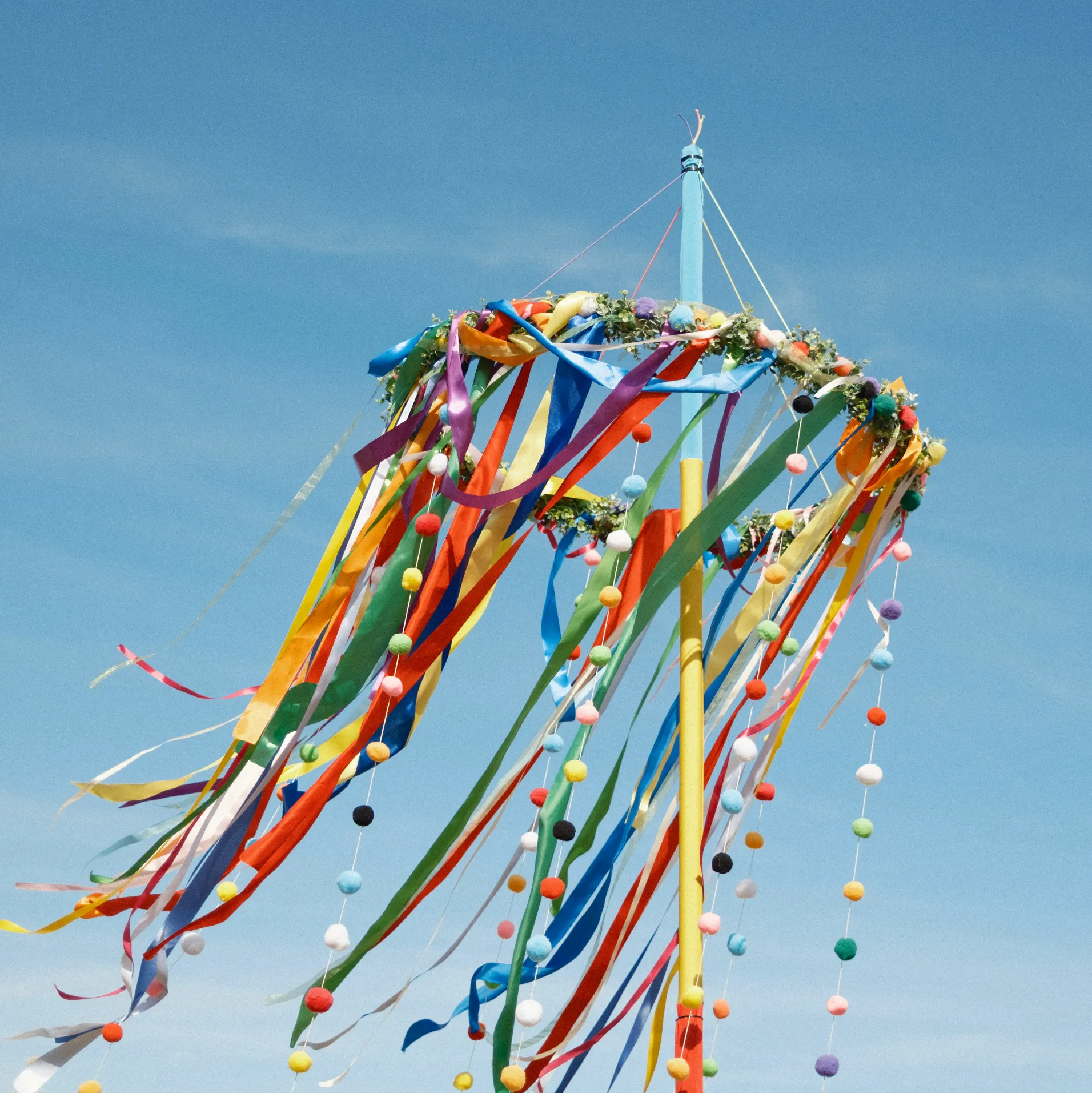 Colourful maypole ribbons and pom-pom garlands flowing in the breeze against a bright blue sky