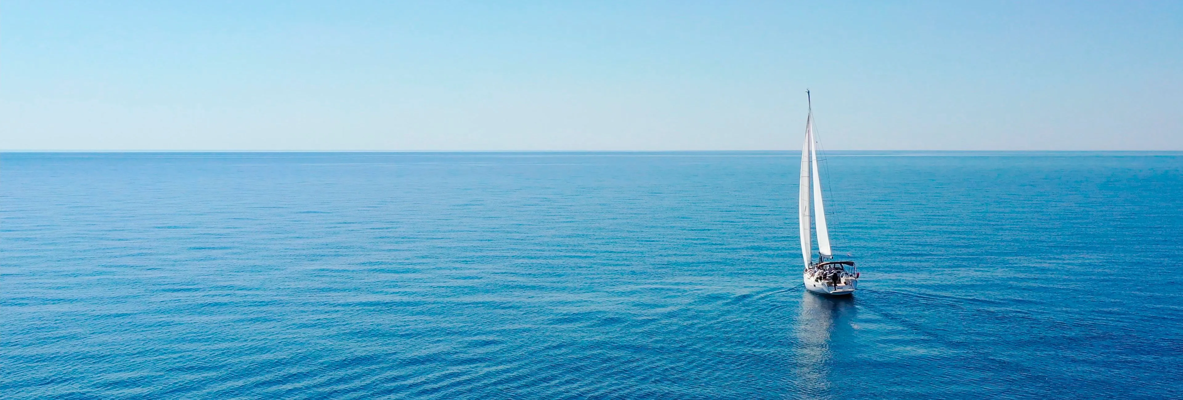 Single sailing boat on a calm blue sea under a clear sky