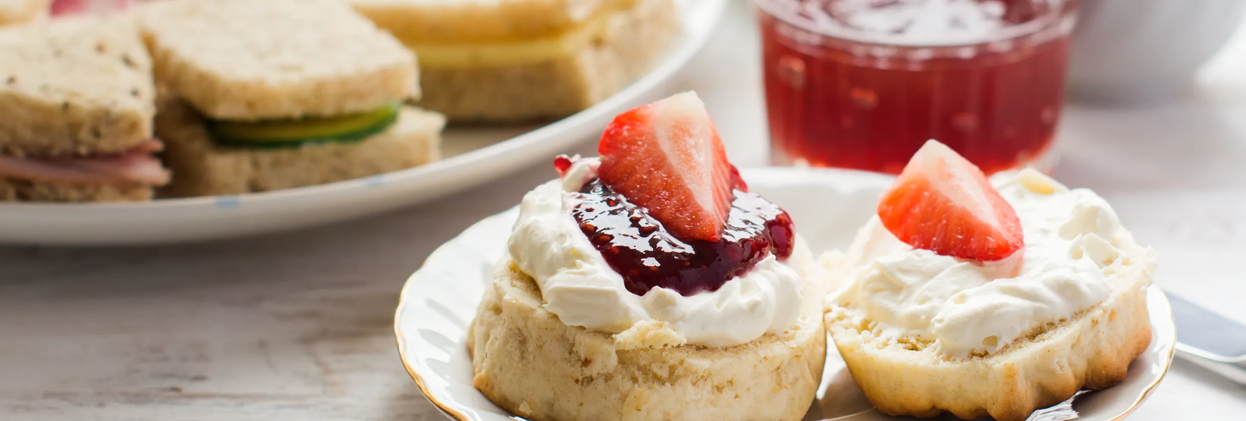 Cream tea with a scone topped with clotted cream, strawberry jam and fresh strawberries, served alongside finger sandwiches and tea.