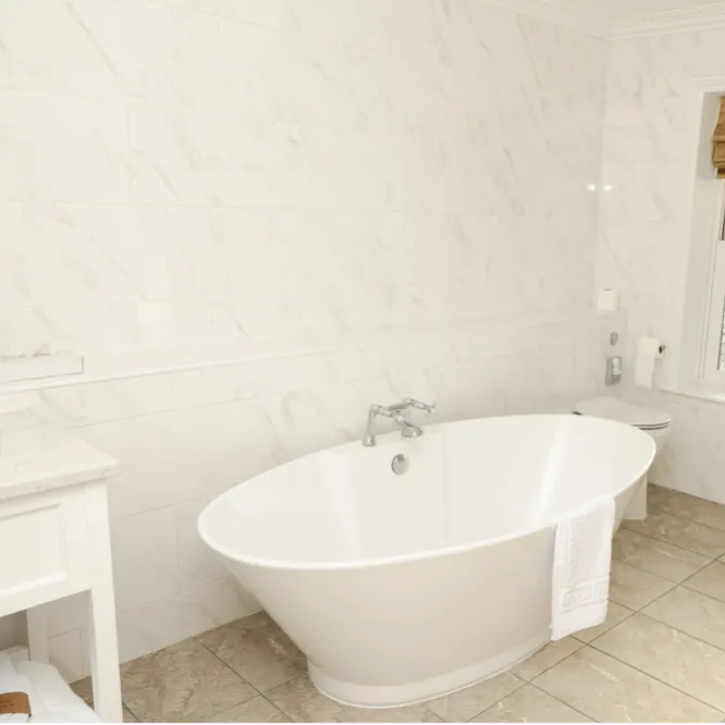 Elegant bathroom with a freestanding white bath, marble-effect wall tiles and a sash window with a Roman blind.