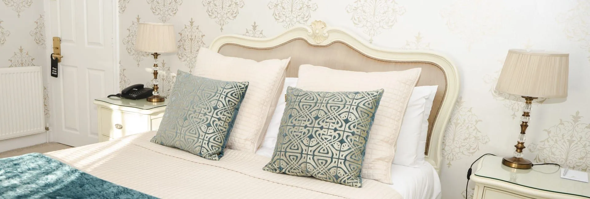 Elegant cream bedroom with an upholstered headboard, patterned blue cushions and matching bedside lamps.
