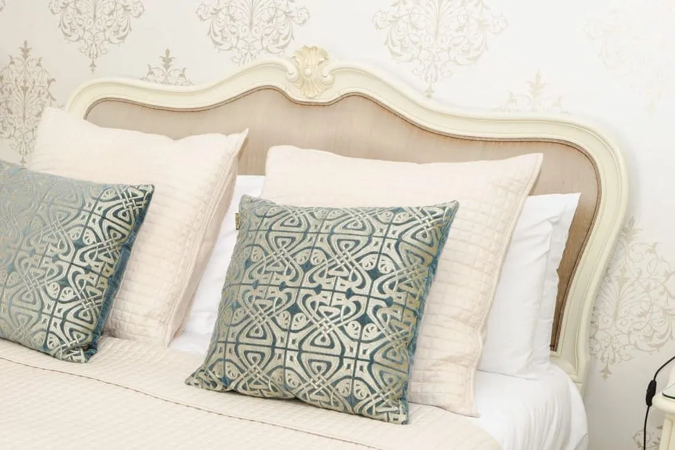 Elegant cream bedroom with an upholstered headboard, patterned blue cushions and matching bedside lamps.