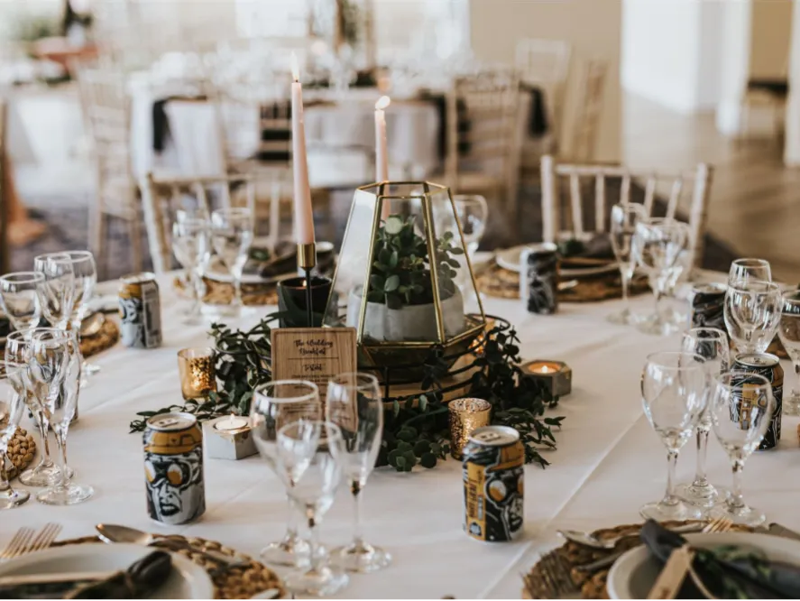 Elegantly dressed reception table with candles, glassware and greenery centrepiece at a wedding venue
