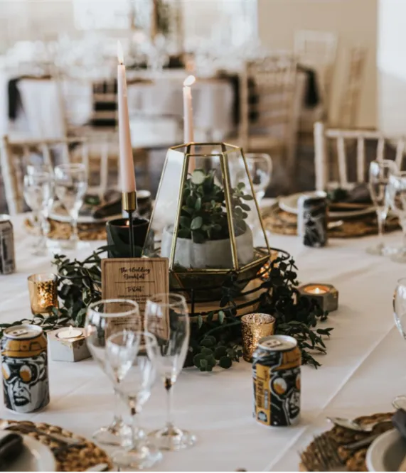 Elegantly dressed reception table with candles, glassware and greenery centrepiece at a wedding venue