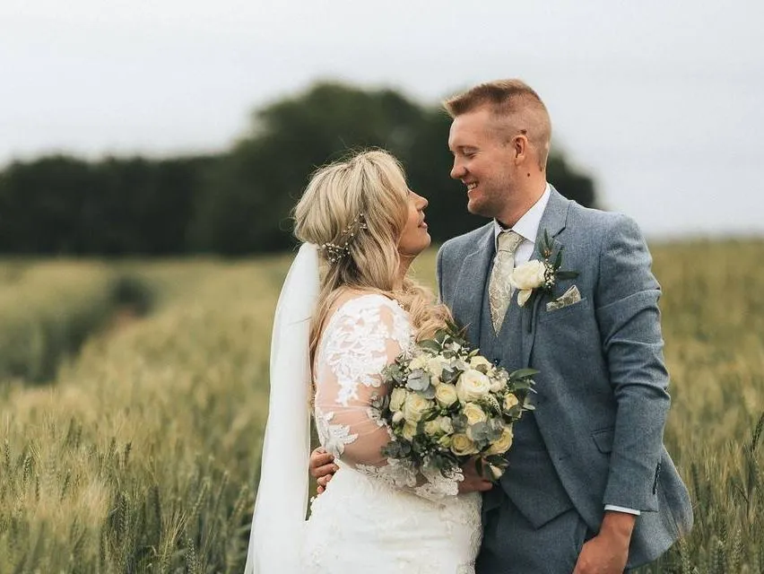 Bride and groom standing together in a field on their wedding day, smiling at each other