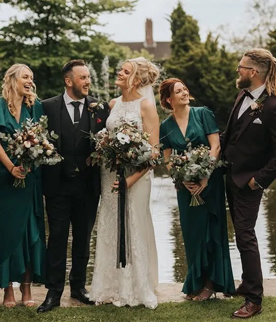 Bride and groom with bridesmaids and groomsmen standing by a lakeside garden