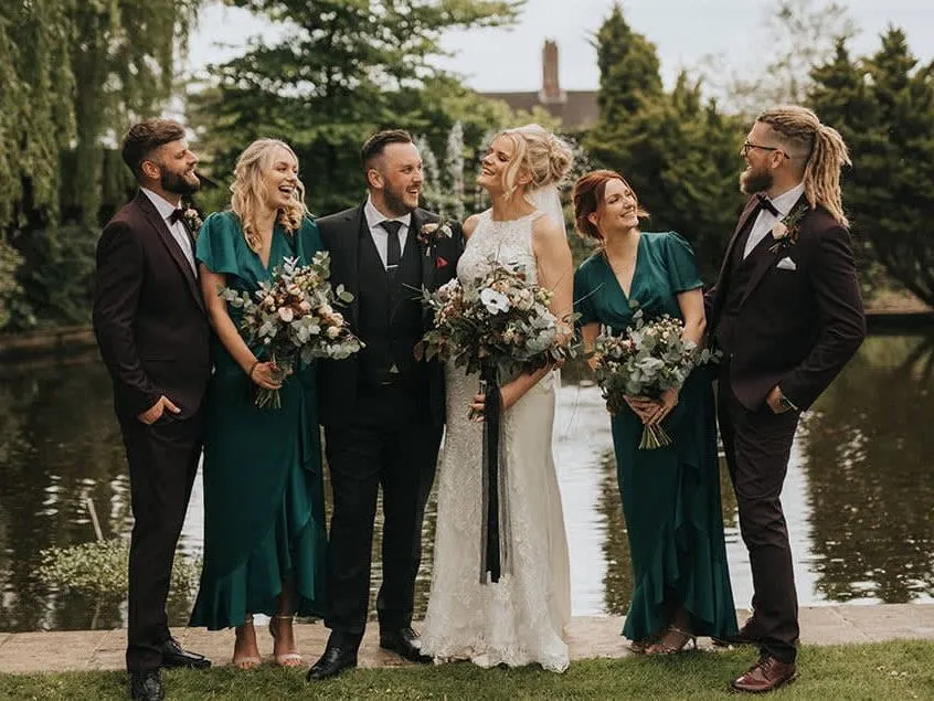 Bride and groom with bridesmaids and groomsmen standing by a lakeside garden