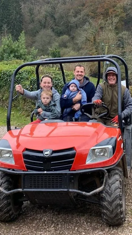 A smiling family sits in a red off-road vehicle, ready for a farm tour.