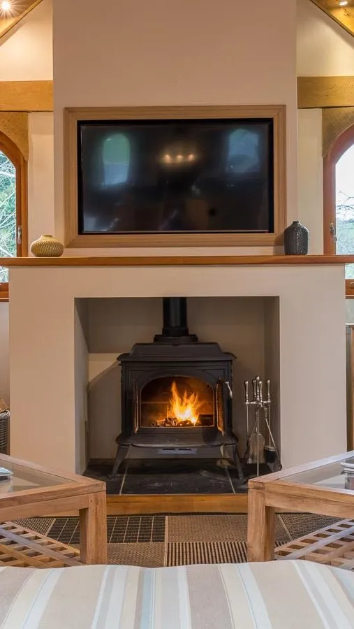 A cosy living room with a wood-burning stove, striped armchairs, wooden beams, and arched windows, creating a warm and inviting countryside retreat.