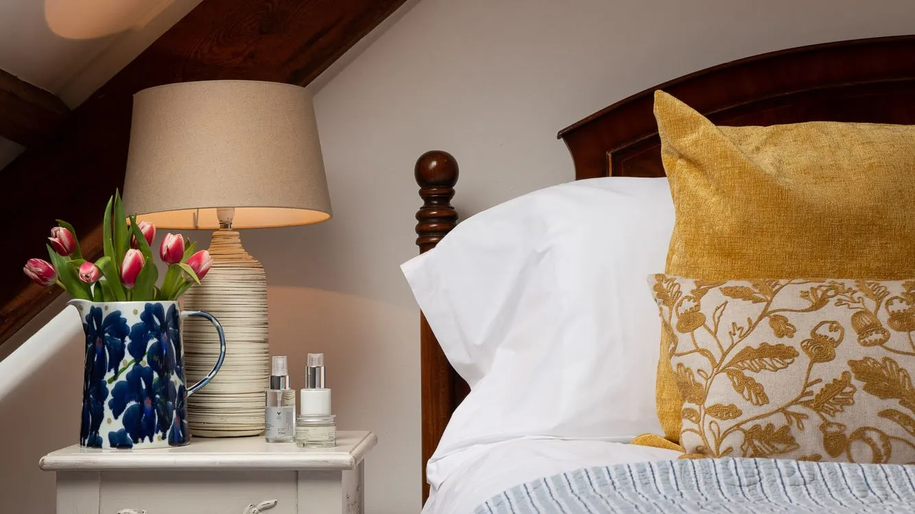 Bed with yellow cushions, vase of tulips on bedside table