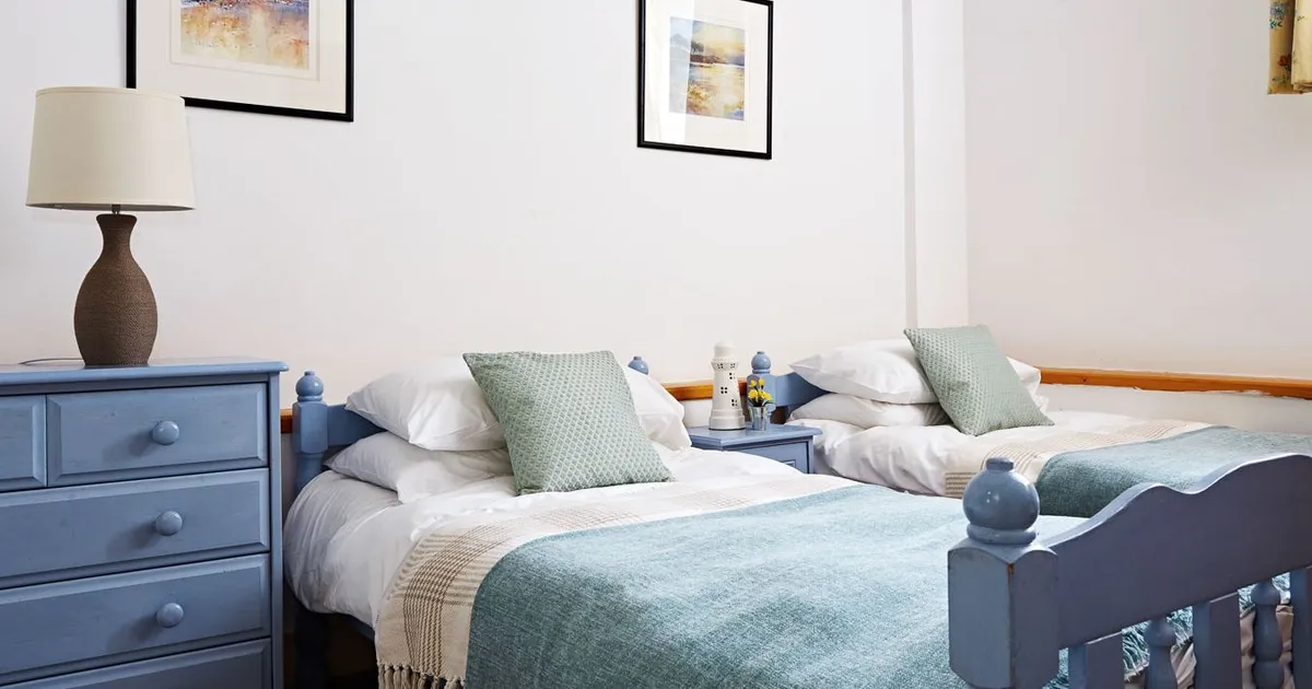 Charming twin bedroom with pastel blue wooden beds, soft green cushions, matching throws, and nautical-themed artwork, creating a cosy and relaxing atmosphere.