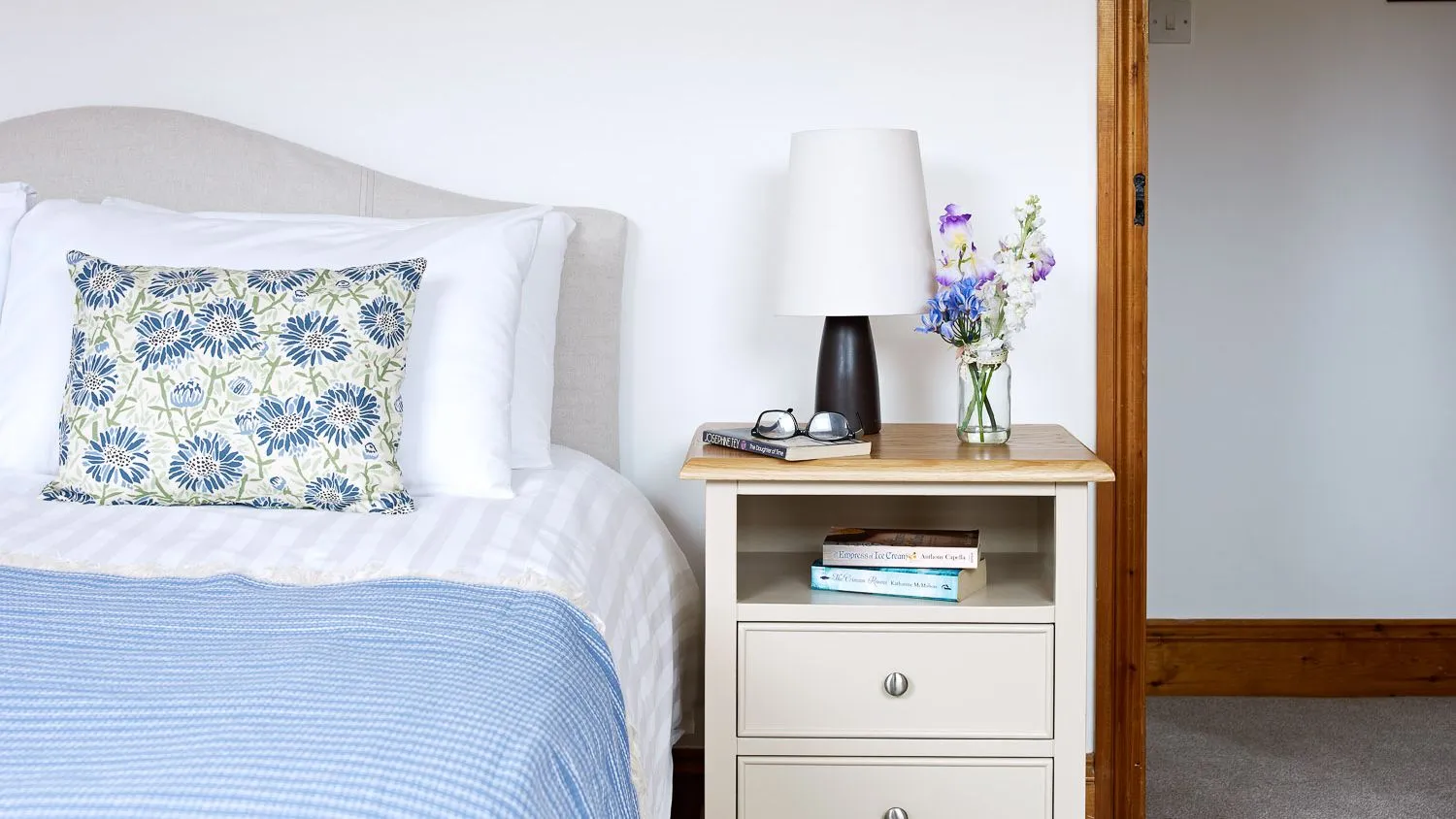 Bed with blue throw, vase of wildflowers on bedside table