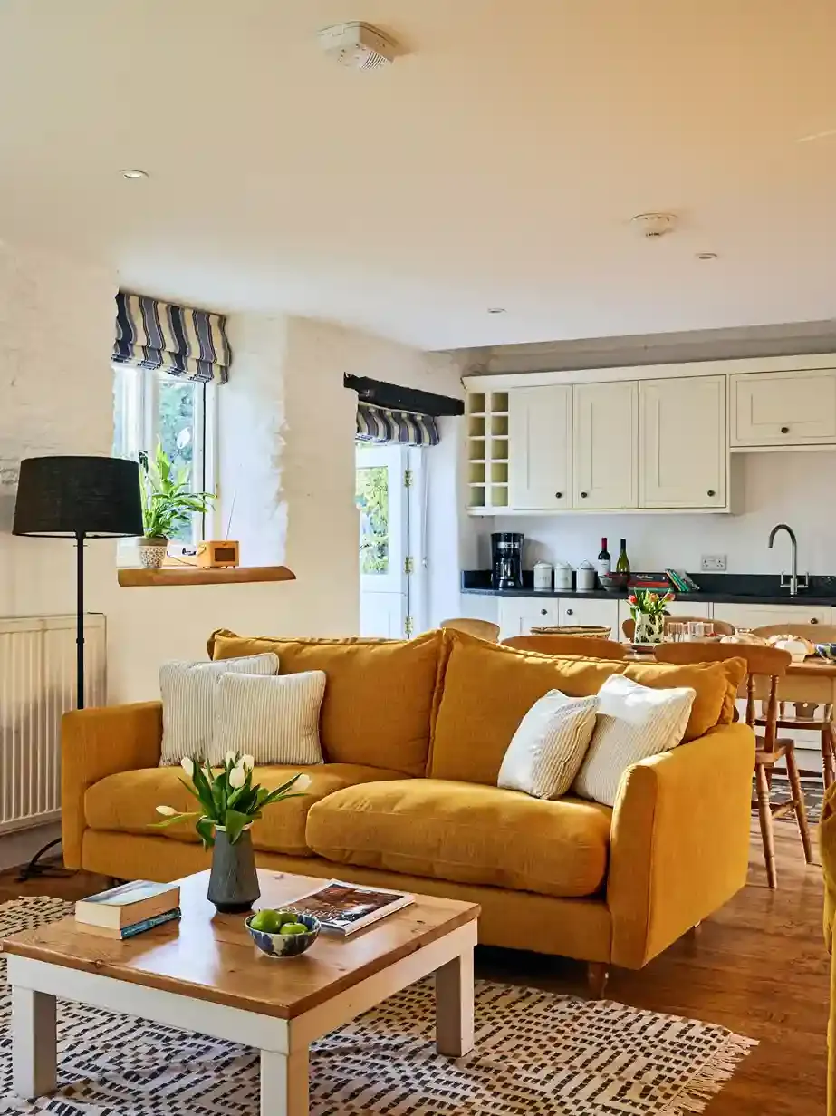 Cosy living room in The Stables at Flear Farm Cottages with mustard sofa, striped blinds, and open-plan kitchen and dining area.