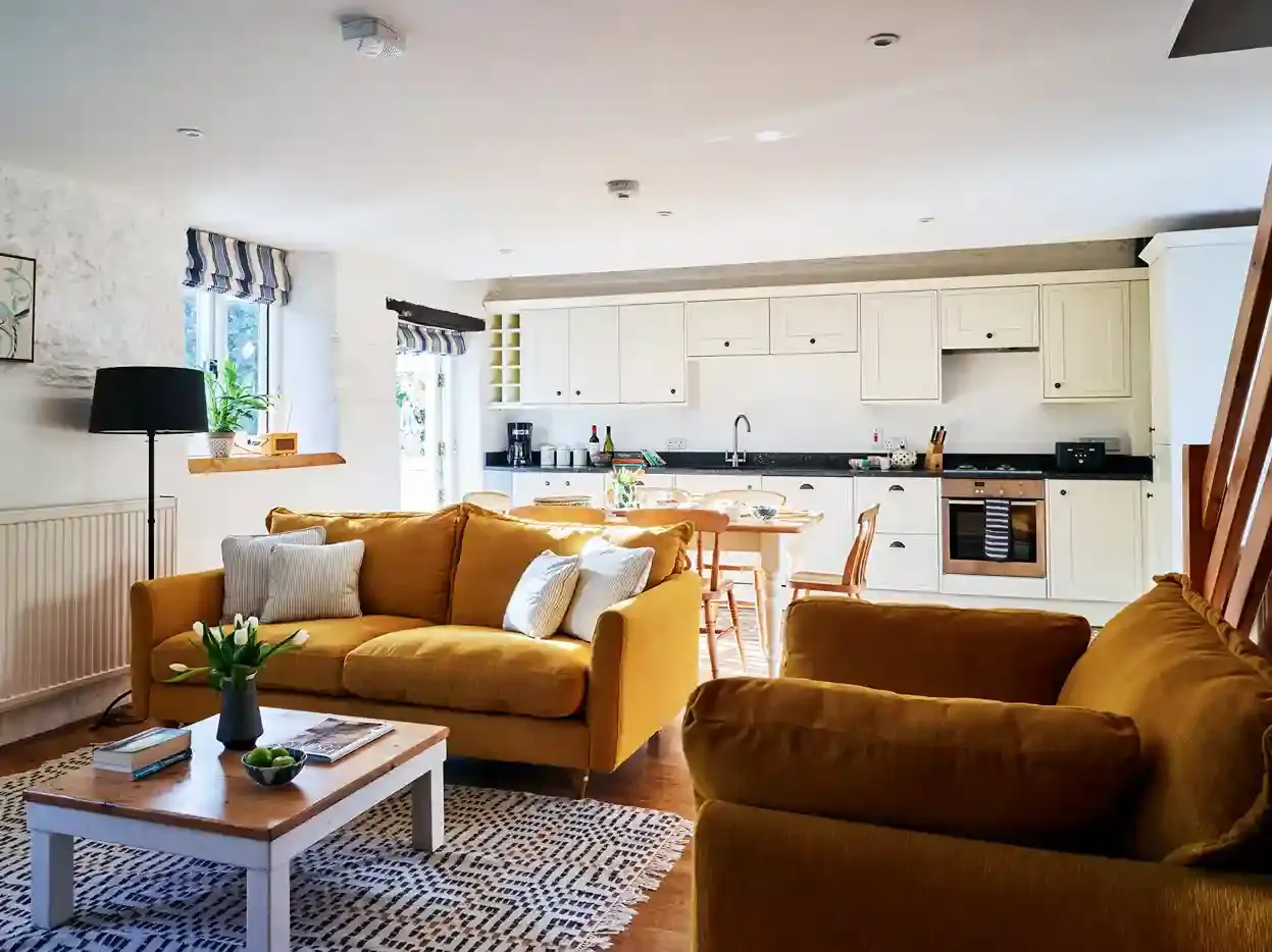 Open-plan living room and kitchen in The Stables at Flear Farm Cottages, with mustard sofas, cream cabinetry and a wooden dining table.