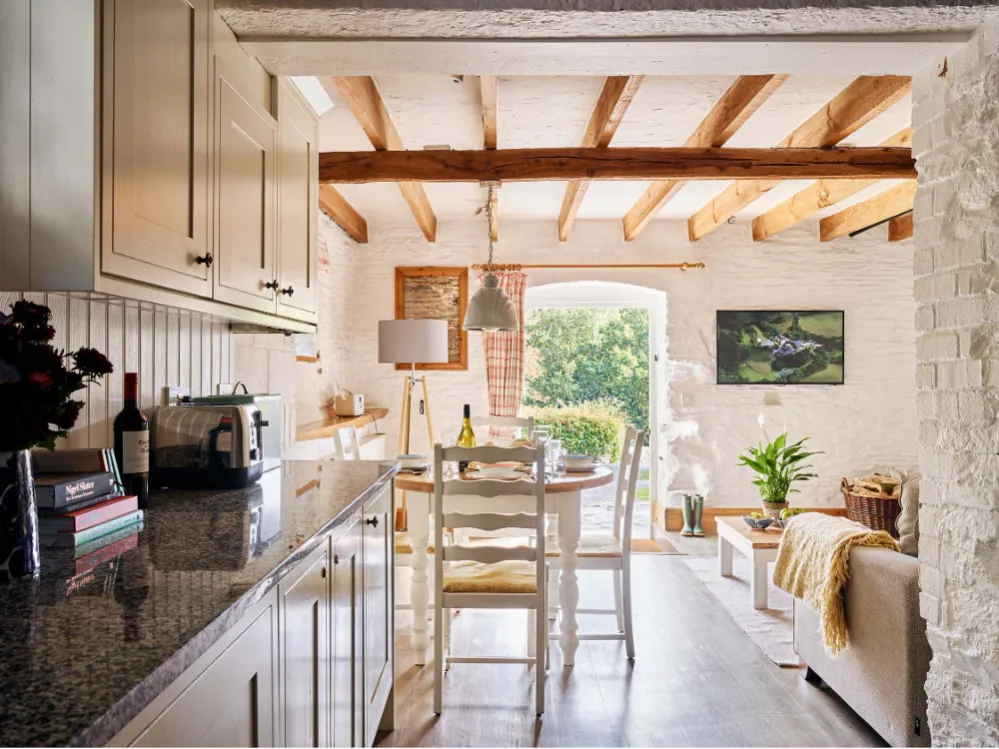 View from Quarry’s kitchen at Flear Farm Cottages through the dining area to open doors, showing the sunlit garden beyond.