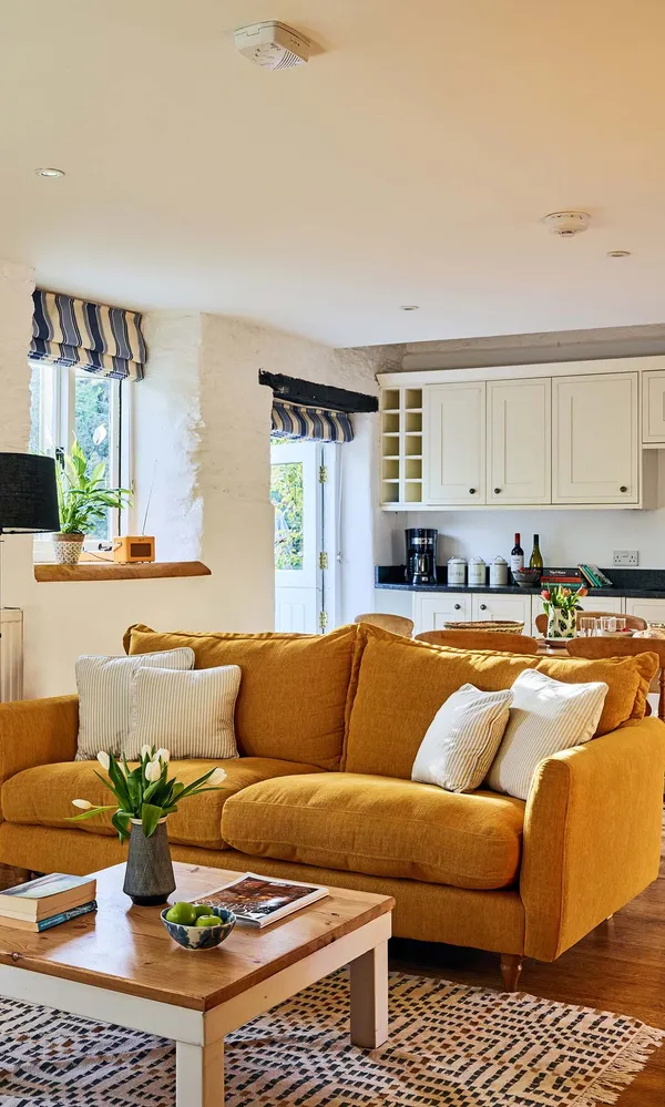 Cosy living room in The Stables at Flear Farm Cottages with mustard sofa, striped blinds, and open-plan kitchen and dining area.