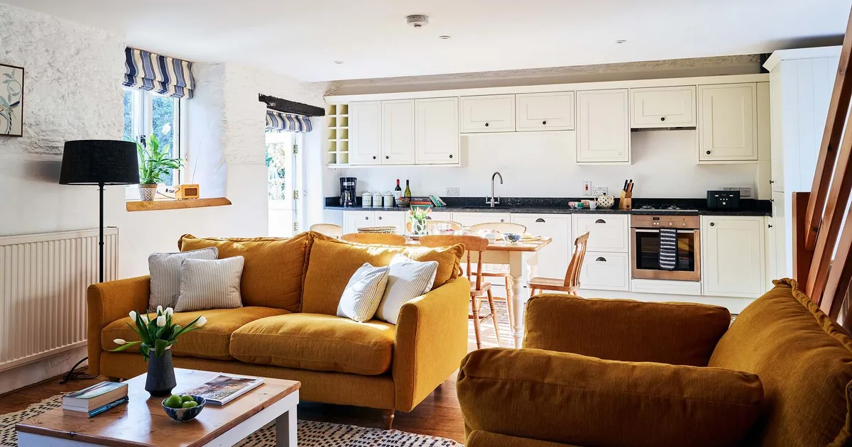 Open-plan living room and kitchen in The Stables at Flear Farm Cottages, with mustard sofas, cream cabinetry and a wooden dining table.