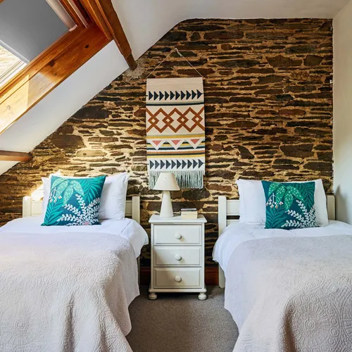 Twin bedroom in Cartwheel at Flear Farm Cottages, with exposed stone wall, skylight, white bedding, and bold green cushions for a fresh touch.