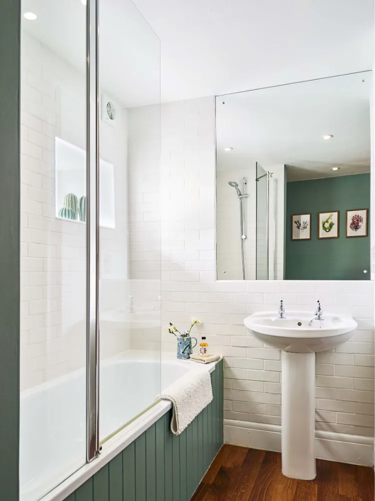 Bright family bathroom in The Stalls at Flear Farm Cottages, featuring a shower over bath, pedestal basin, wood flooring, and green panelled bath side.