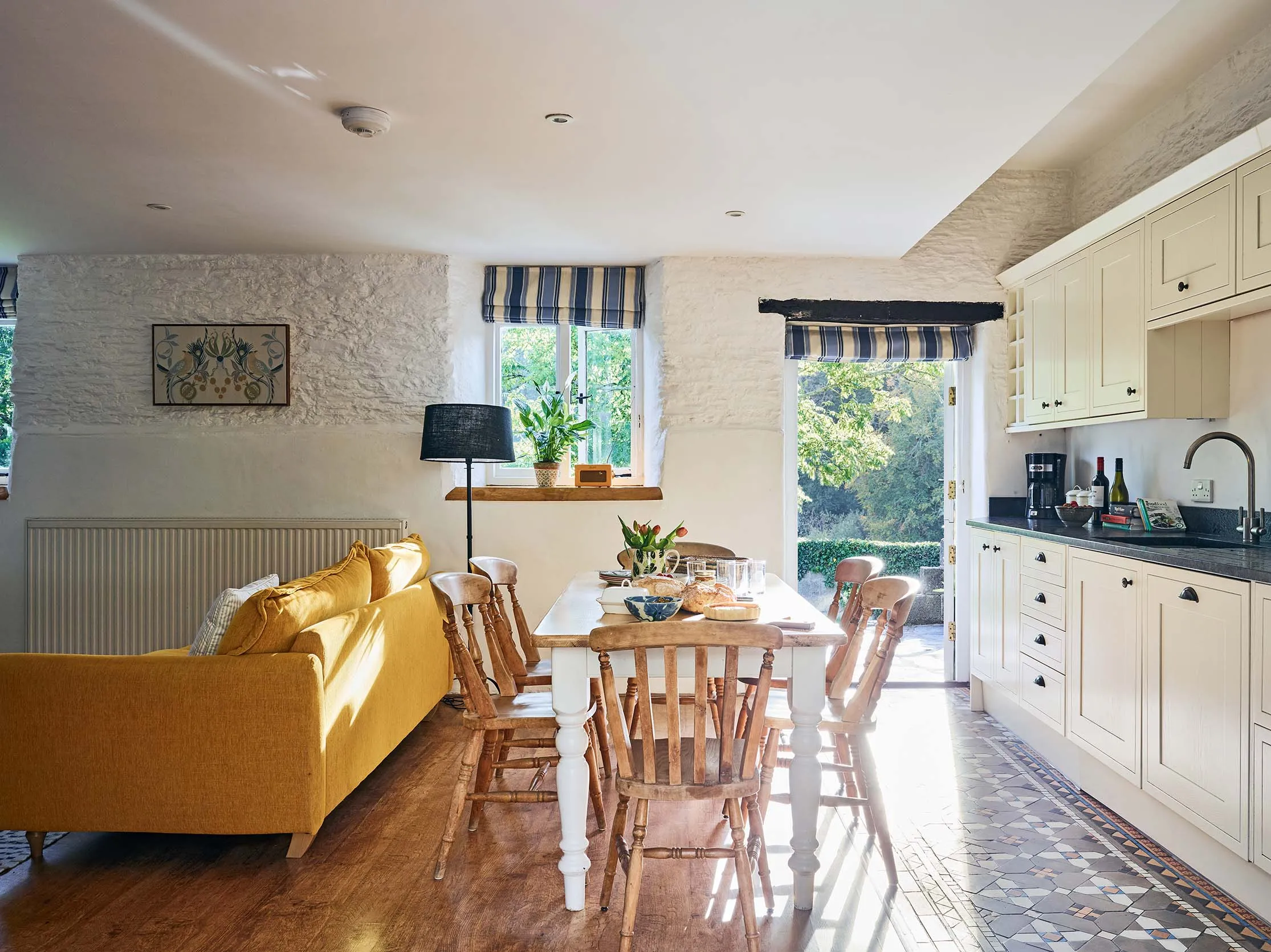 Dining area and kitchen in The Stables at Flear Farm Cottages, with wooden chairs, shaker-style units, and doors opening to the garden.