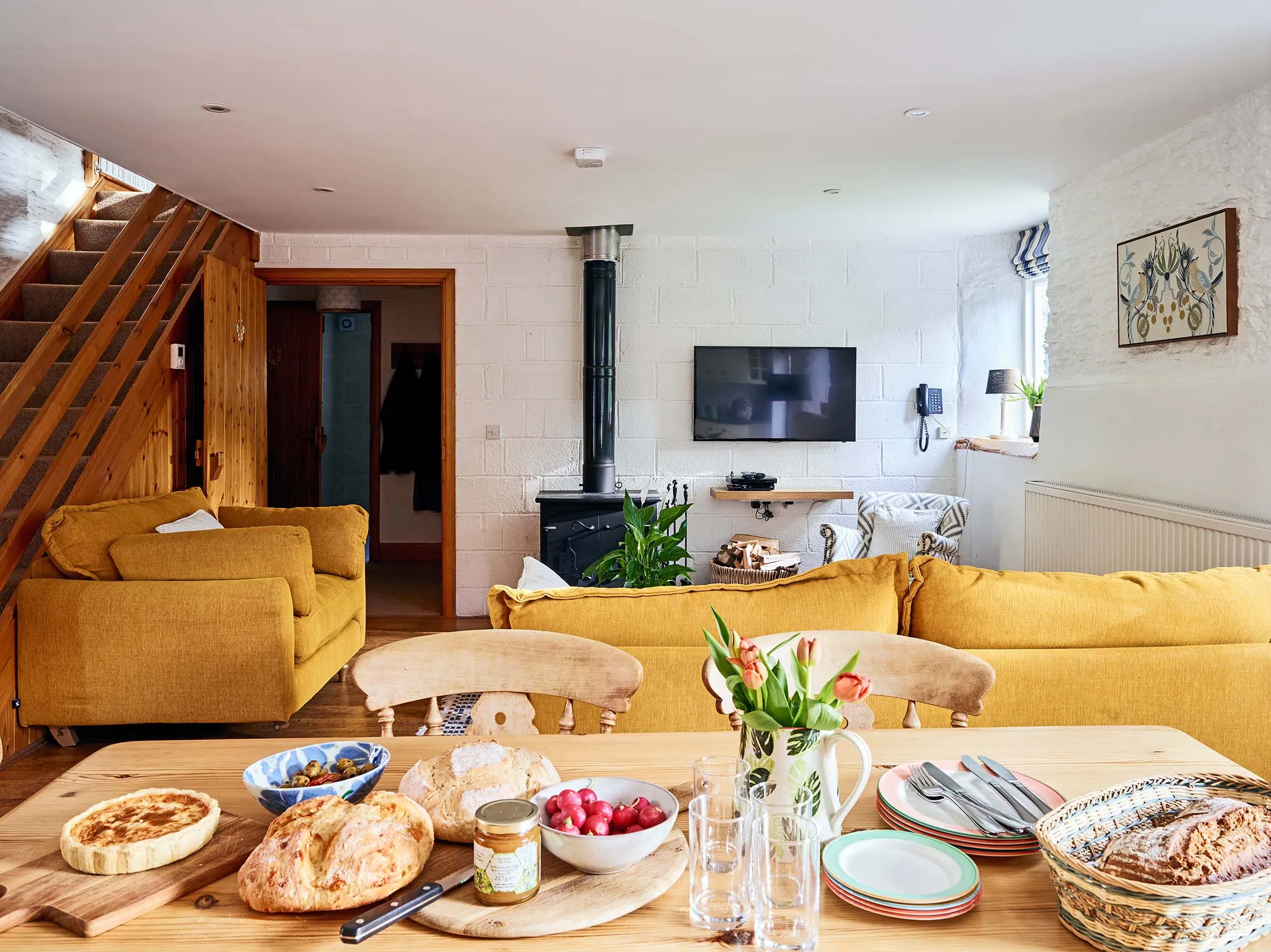 View from the kitchen table to the living room in The Stables at Flear Farm Cottages, with mustard sofas and a wood-burning stove.