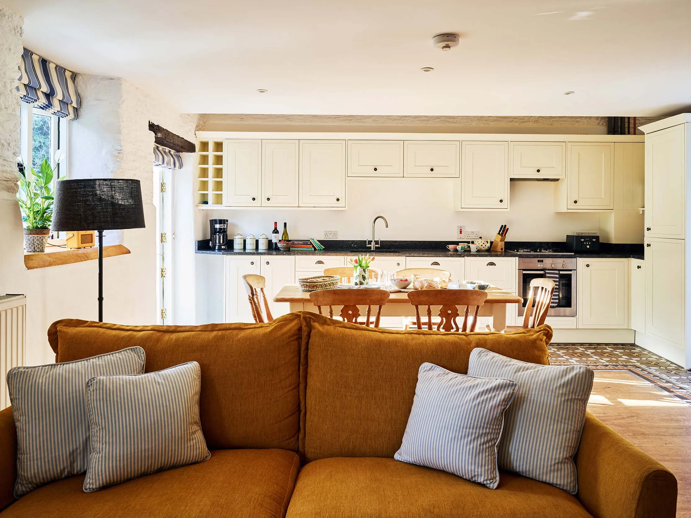 The Stables at Flear Farm Cottages, with a mustard sofa in the foreground and cream shaker-style kitchen with dining table in the background.