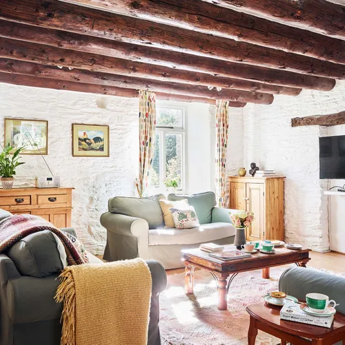 Portrait view of the Granary’s living room at Flear Farm Cottages, with exposed beams, soft seating, rustic furnishings, and sunlight streaming in.