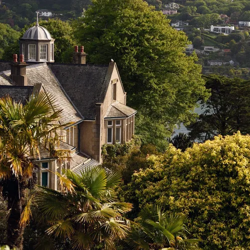 Overbeck’s Garden in South Devon featuring dense greenery, palm trees, and a coastal view across the water to hillside villages.
