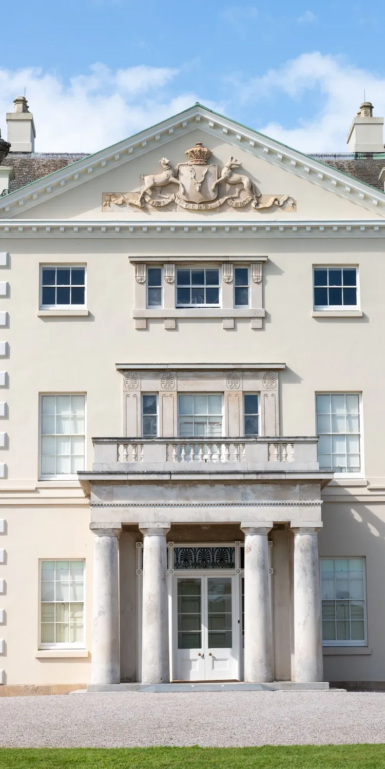 Central entrance of Saltram House in Plymouth, with four stone columns, tall sash windows and a carved crest beneath the pediment.